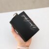 Una mano sosteniendo un frasco negro con escritura cursiva, sobre una superficie blanca.